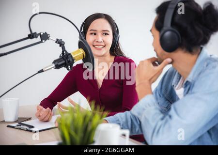 Deux hôtes asiatiques radio enregistrement podcast dans le studio de diffusion, femme asiatique parlant sur le microphone avec l'homme en ligne à la maison. Banque D'Images