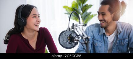 Deux hôtes asiatiques radio enregistrement podcast dans le studio de diffusion, femme asiatique parlant sur le microphone avec l'homme en ligne à la maison. Banque D'Images