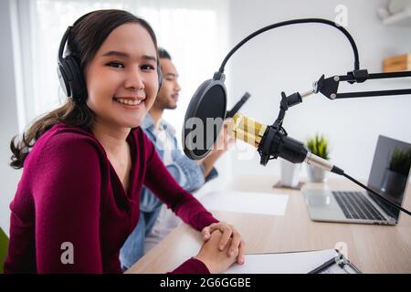 Deux hôtes asiatiques radio enregistrement podcast dans le studio de diffusion, femme asiatique parlant sur le microphone avec l'homme en ligne à la maison. Banque D'Images