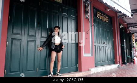 Chinoise asiatique Femme modèle Poser actrice portant Black Leather Jacket blanc Chemisier debout dans la porte en bois d'une maison du patrimoine Bangkok Thaïlande Banque D'Images