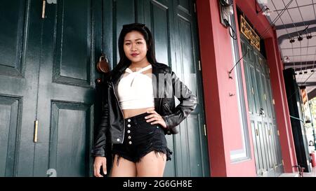 Chinoise asiatique Femme modèle Poser actrice portant Black Leather Jacket blanc Chemisier debout dans la porte en bois d'une maison du patrimoine Bangkok Thaïlande Banque D'Images