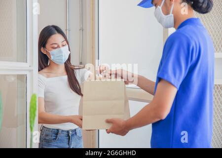 Liveur portant un masque, livrez le sac de nourriture au client, femme pendant le confinement de la ville en raison de coronaviris ou covid19 Banque D'Images