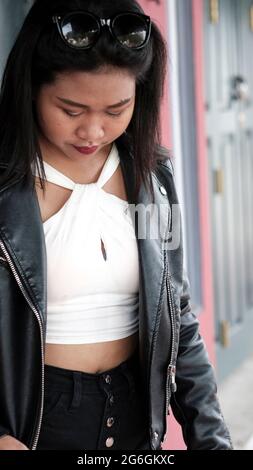 Chinoise asiatique Femme modèle Poser actrice portant Black Leather Jacket blanc Chemisier debout dans la porte en bois d'une maison du patrimoine Bangkok Thaïlande Banque D'Images