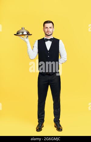 Portrait complet d'un élégant plateau de rangement de serveur avec couvercle prêt à servir sur fond jaune. Restaurant, concept horeca Banque D'Images