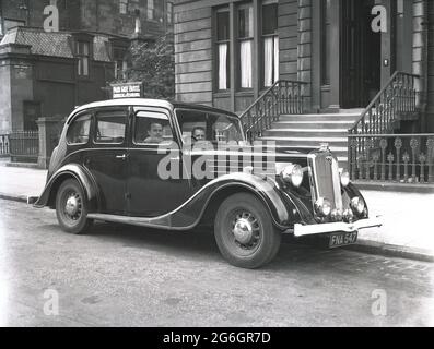 Années 1950, historique, deux hommes assis dans une voiture de l'époque garés devant les marches de l'entrée de l'hôtel Park Gate, Park Circus, Glasgow, Écosse, Royaume-Uni. Construit entre 1855 et 1863, la région a présenté un cirque symétriquement arrangé de grandes maisons mitoyennes élégantes, de style italien, 3 étages et sous-sol, conçu par l'architecte Charles Wilson. Banque D'Images