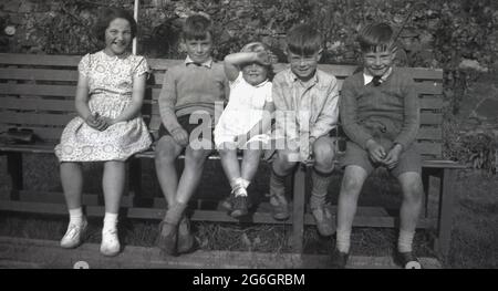 1950s, historique, groupe de jeunes enfants, frères et sœurs, assis ensemble dans une ligne sur un banc en bois, Angleterre, Royaume-Uni. Les garçons typiques, qui ont l'air délabré après une journée d'école. Banque D'Images