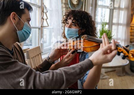 Une femme heureuse joue du violon sous les instructions d'un professeur de musique dans un masque pendant le coronavirus à la maison Banque D'Images