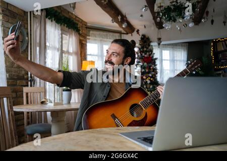 Jeune hispanique jouant de la guitare à la maison avec un ordinateur portable Banque D'Images