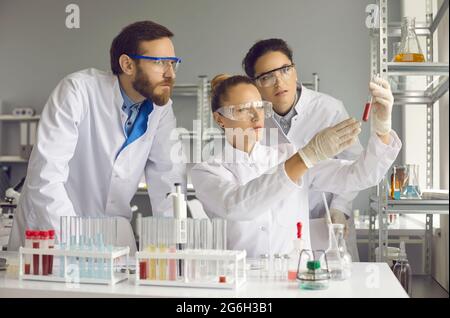 Les jeunes scientifiques regardent un tube à essai avec une substance rouge en laboratoire. Banque D'Images