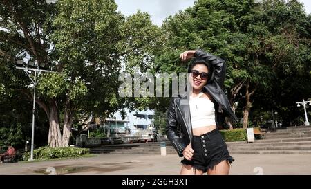 Happy Asian Girl porte des lunettes de soleil Black Leather Jacket Black Chemisier blanc comme modèle causal Walking dans le parc Bangkok Thaïlande Banque D'Images