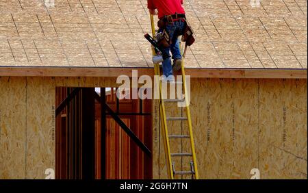 Un ouvrier de la construction monte sur le chantier de l'échelle à la maison en cours de construction Banque D'Images