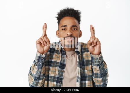 Gros plan de l'homme nerveux plein d'espoir, un gars afro-américain croiser les doigts bonne chance, en attendant que le rêve se réalise, en faisant du vœu, debout dans une chemise à carreaux Banque D'Images