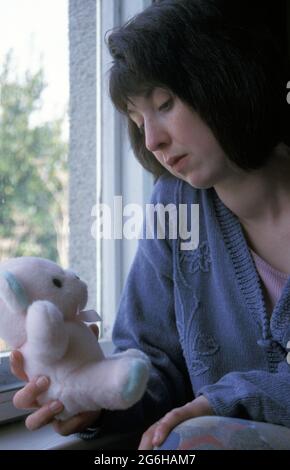 femme malheureuse assise par la fenêtre tenant l'ours en peluche Banque D'Images