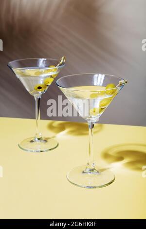 Deux verres de cocktails martini aux olives vertes, sur fond d'ombre de plantes tropicales Banque D'Images