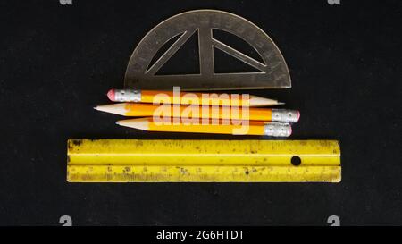 Trois crayons, Protractor, et une règle sur un fond noir Banque D'Images
