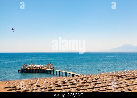 Les personnes se baignant, se bronzer ou faire d'autres activités sur la plage. Grand groupe de parasols en paille sur le sable. Les personnes bronzant sur un quai en bois et Banque D'Images