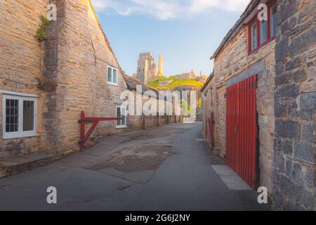 Les ruines médiévales au sommet d'une colline dans le village pittoresque et historique de Corfe Castle, Dorset, Angleterre avec coucher de soleil à l'heure d'or ou lever de soleil lumière d'été. Banque D'Images
