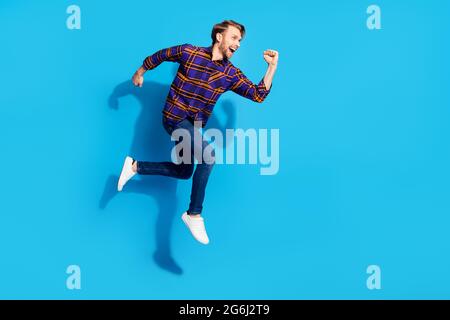 Photo d'un jeune gentleman habillé à carreaux chemise sourire sautant courir isolé bleu couleur arrière-plan Banque D'Images
