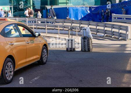 Deux bagages à roulettes négligés se trouvent à côté d'une voiture de taxi jaune garée près de la passerelle Banque D'Images