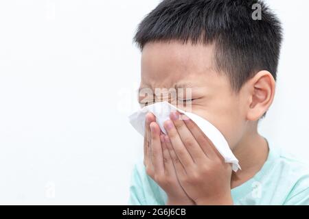 Petit garçon asiatique soufflant son nez ou nettoyant le nez avec du tissu. Le petit garçon était malade et éternuait sur fond blanc isolé. Banque D'Images