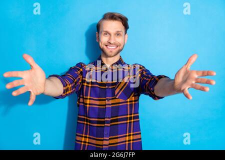 Portrait d'un joli homme joyeux portant une chemise à carreaux vous offrant un soutien-gorge chaud isolé sur un fond bleu vif Banque D'Images