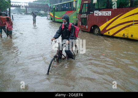 Un homme livrant de la nourriture passe par l'eau de pluie sur son vélo avec une parcelle pendant une grosse déverse. Quelques heures de pluie créent de l'engorgement dans les rues car le système d'égouts et de drains n'est pas nettoyé et entretenu correctement. Dhaka, Bangladesh. Banque D'Images