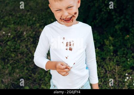 Garçon montrant des taches de chocolat sur des vêtements blancs, de la saleté sur son visage. Photo de haute qualité Banque D'Images