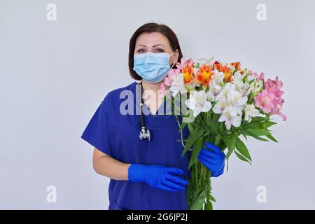 Femelle medic en bleu uniforme masque médical avec bouquet de fleurs sur fond clair Banque D'Images