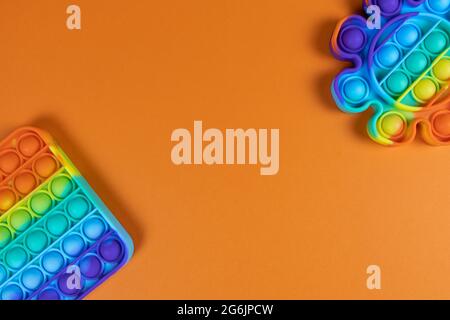 Les jouets anti-stress le pop, simple bosselé, sur fond orange, espace de copie. Concept de divertissement à la mode pour les enfants de violon, jouets sensoriels pour le développement Banque D'Images