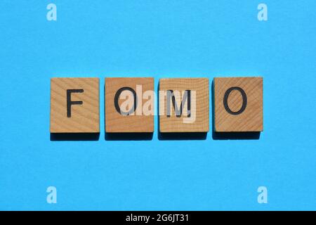 FOMO acronyme, peur of Missing Out dans des lettres de l'alphabet en bois isolées sur fond bleu Banque D'Images