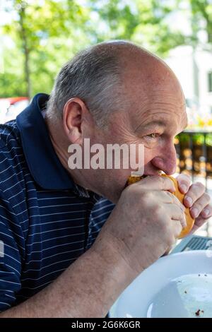 Un homme mange un sandwich au filet pané à Sahm's Ale House, un café en plein air de Carmel, village de WestClay dans l'Indiana. Banque D'Images