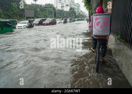 Un homme livrant de la nourriture passe par l'eau de pluie sur son vélo avec une parcelle pendant une grosse déverse. Quelques heures de pluie créent de l'engorgement dans les rues car le système d'égouts et de drains n'est pas nettoyé et entretenu correctement. Dhaka, Bangladesh. Banque D'Images