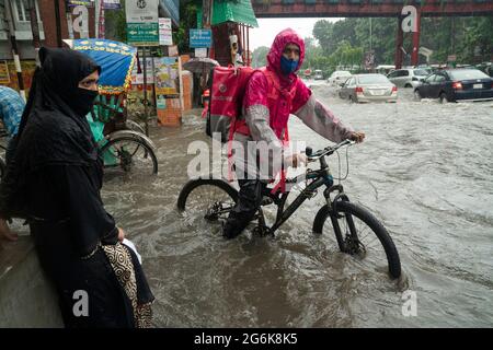 Un homme livrant de la nourriture passe par l'eau de pluie sur son vélo avec une parcelle pendant une grosse déverse. Quelques heures de pluie créent de l'engorgement dans les rues car le système d'égouts et de drains n'est pas nettoyé et entretenu correctement. Dhaka, Bangladesh. Banque D'Images