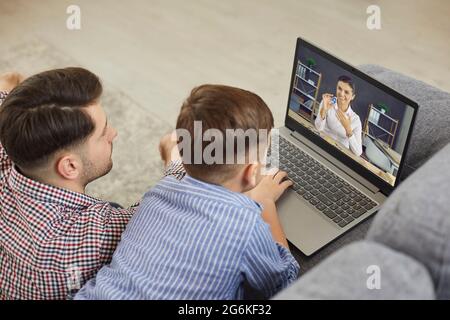 Père et fils regardant un ordinateur portable tout en ayant une leçon en ligne avec un professeur d'anglais Banque D'Images