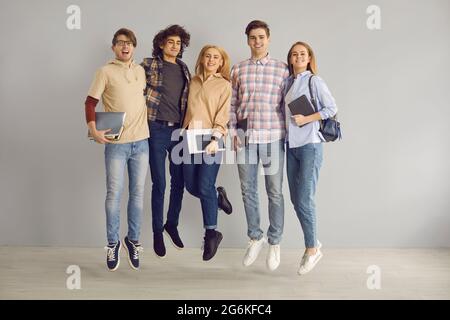 Portrait d'un groupe de jeunes filles et de garçons gais qui sautent sur un fond de mur gris. Banque D'Images