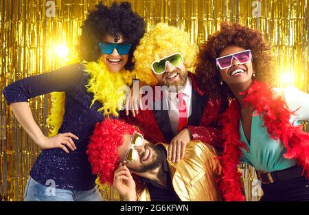 Souriant et souriant, des amis insouciants posent pour un appareil photo dans une perruque de cheveux de fête Banque D'Images