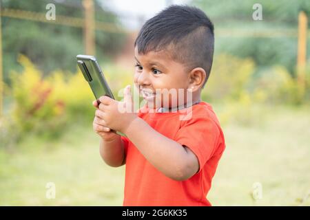 Portrait d'un enfant indien chubby heureux surpris en riant en regardant dans le téléphone mobile - concept d'enfants dépendance mobile, Internet et la technologie. Banque D'Images