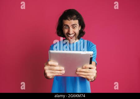 Inshaven homme excité jouant en ligne jeu sur ordinateur tablette isolé sur fond rose Banque D'Images