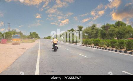 07 juillet 2021- Reengus, Sikar, Inde. Moto passant par la route asphaltée avec le chemin du boulevard et le fond horizontal nuageux du ciel. Banque D'Images