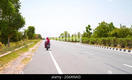 07 juillet 2021- Reengus, Sikar, Inde. Longue route asphaltée et véhicules traversant la forêt. Route de transport asphaltée avec boulev vert Banque D'Images