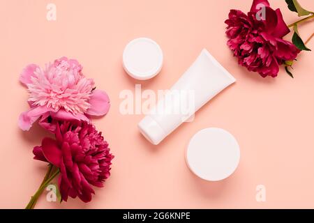 Produits cosmétiques crème gel shampooing baume dans différentes bouteilles sur fond rose avec fleurs fraîches pivoines Banque D'Images