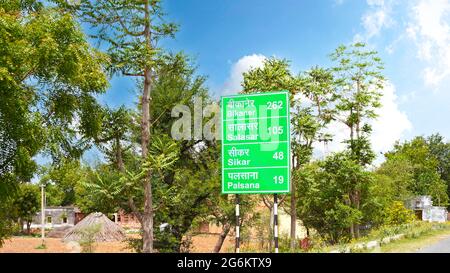07 juillet 2021- Reengus, Sikar, Inde. Plan de près du panneau d'affichage vert avec texte écrit attrayant pour les villes. Quelques arbres et ciel nuageux également contre Banque D'Images