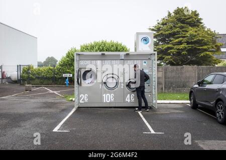 Un homme attend que son linge se termine dans une laverie en plein air dans un parking de supermarché à Ploussgasnou, en France Banque D'Images