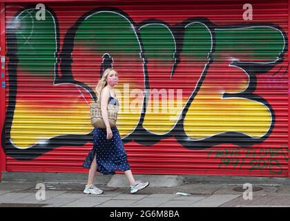 Une femme masquée passe devant un panneau de graffiti avec le mot AMOUR écrit sur les enseignes de magasin dans l'Ouest de Londres Banque D'Images
