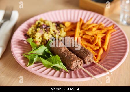 Repas végétalien sur assiette avec Kofta Kebabs à base de plantes avec frites de pommes de terre douces et couscous et salade Banque D'Images