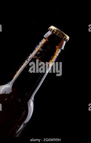 Bouteille de bière en verre foncé avec gouttes de condensation sur fond noir. Banque D'Images