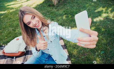 heureux étudiant montrant le pouce vers le haut tout en emportant le selfie dans le parc Banque D'Images