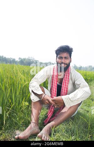 Jeune agriculteur rural indien assis dans le champ agricole Banque D'Images
