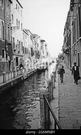 Une photographie noir et blanc du début du XXe siècle montrant un garçon et un homme marchant au bord d'un canal à Venise, en Italie. Banque D'Images