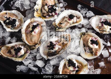 Huîtres sales servies sur un lit de glace concassée : huîtres crues recouvertes de caviar, échalotes hachées et crème fraîche Banque D'Images